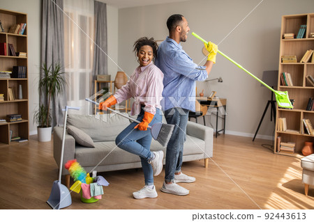 Happy African American Couple Doing Housework Cleaning House Singing Indoors 92443613