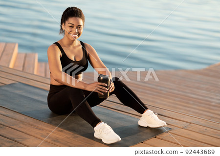 Cheerful african american athletic woman drinking water, exercising outdoors Cheerful african american athletic woman drinking water, exercising outdoors 92443689