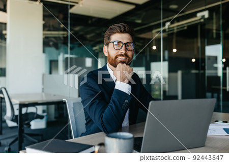 Dreamy businessman sitting at workplace in office and thinking of new business strategy, looking aside and smiling Dreamy businessman sitting at workplace in office and thinking of new business strategy, looking aside and smiling 92443847