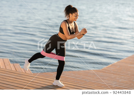 Active black woman doing workout outdoors, using resistance band Active black woman doing workout outdoors, using resistance band 92443848