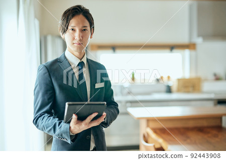 A home sales businessman standing with a tablet in front of the kitchen A home sales businessman standing with a tablet in front of the kitchen 92443908