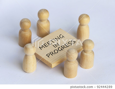 Wooden people figures having business meeting with meeting in progress text on wooden table. 92444289