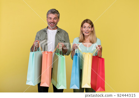Big sale and shopping with pleasure. Excited middle aged spouses holding many colored packages in hands Big sale and shopping with pleasure. Excited middle aged spouses holding many colored packages in hands 92444315