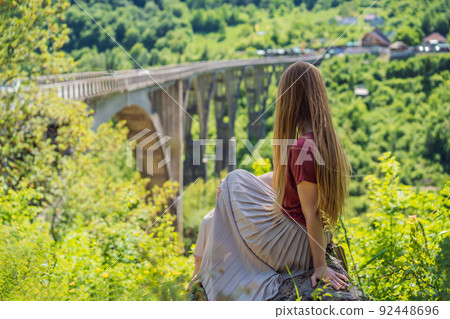 Montenegro. Woman tourist in background of Dzhurdzhevich Bridge Over The River Tara. Travel around Montenegro concept. Sights of Montenegro Portrait of a disgruntled girl sitting at a cafe table 92448696