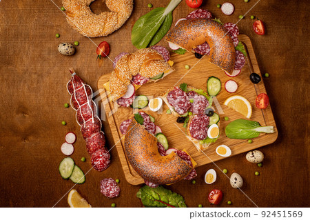 Set of fresh bagels with Salami, radish, cucumber. Top view. Wooden background Set of fresh bagels with Salami, radish, cucumber. Top view. Wooden background 92451569