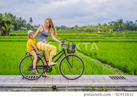 Mother and son ride a bicycle on a rice field in Ubud, Bali. Travel to Bali with kids concept Mother and son ride a bicycle on a rice field in Ubud, Bali. Travel to Bali with kids concept 92451632