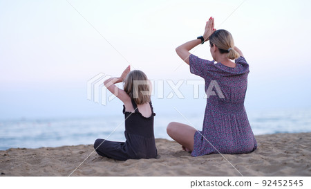 Mother and daughter do yoga meditate in lotus position on beach. Mother and daughter do yoga meditate in lotus position on beach. 92452545