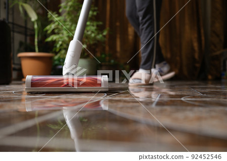Cordless vacuum cleaner with turbo brush cleans tiles in living room Cordless vacuum cleaner with turbo brush cleans tiles in living room 92452546