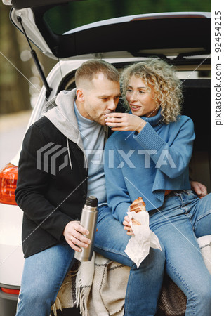 Romantic couple sitting in a trunk of white car in a forest with a tea and croissants 92454215