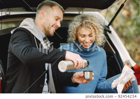 Romantic couple sitting in a trunk of white car in a forest with a tea and croissants 92454234