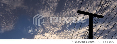 The contour of barbed wire against the background of beautiful clouds and sky 92454509