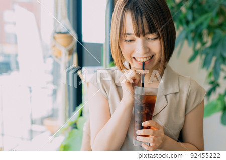 Woman drinking iced coffee at a cafe Woman drinking iced coffee at a cafe 92455222