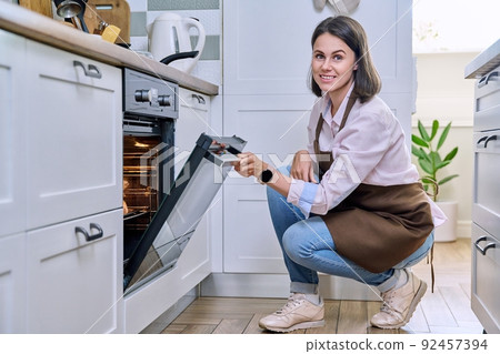 Young woman cooking food in the oven at home in the kitchen. Young woman cooking food in the oven at home in the kitchen. 92457394
