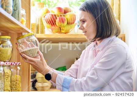 Young woman in kitchen with containers jars of food Young woman in kitchen with containers jars of food 92457420