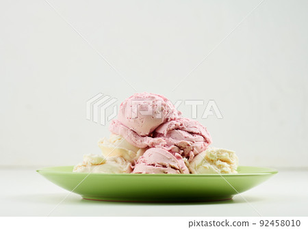 Vanilla and raspberry ice cream scoops on a round green plate 92458010
