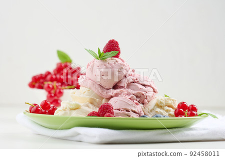 Vanilla and raspberry ice cream scoops on a round green plate 92458011