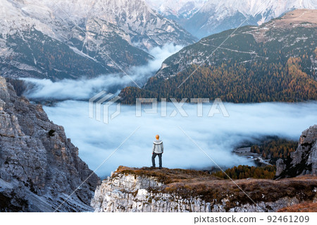 A tourist stands over the fog at the edge of a cliff in the Dolomites mountains A tourist stands over the fog at the edge of a cliff in the Dolomites mountains 92461209
