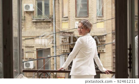 a blonde woman in a white suit on the balcony against the background of the city a blonde woman in a white suit on the balcony against the background of the city 92461211