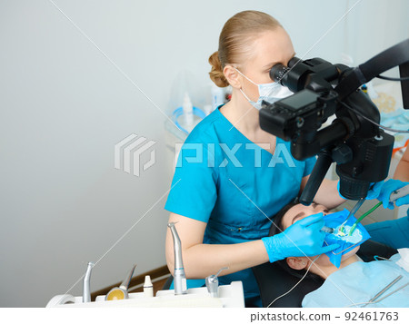 Female dentist using dental microscope Female dentist using dental microscope 92461763