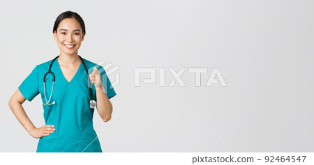 Covid-19, healthcare workers, pandemic concept. Confident smiling asian professional doctor, nurse in scrubs pointing finger at camera, inviting for check-up or vaccination, give recommendation Covid-19, healthcare workers, pandemic concept. Confident smiling asian professional doctor, nurse in scrubs pointing finger at camera, inviting for check-up or vaccination, give recommendation 92464547