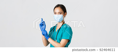 Covid-19, coronavirus disease, healthcare workers concept. Professional confident asian female doctor, nurse in medical mask and scrubs, put on rubber gloves for examination, white background 92464611