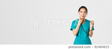 Covid-19, healthcare workers and preventing virus concept. Cute smiling asian female intern learn how listen lungs with stethscope, doctor examine patient, looking thoughtful upper left corner 92464625