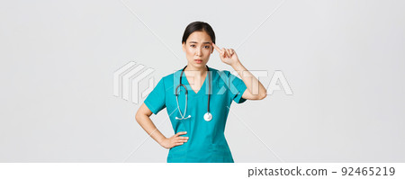 Covid-19, healthcare workers, pandemic concept. Annoyed skeptical asian female nurse or doctor scolding someone acting crazy or stupid, roll finger over temple with judgemental face 92465219