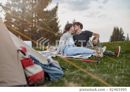 Happy man and woman kissing on grass at tent while resting at rural nature. Camping at wood. 92465995