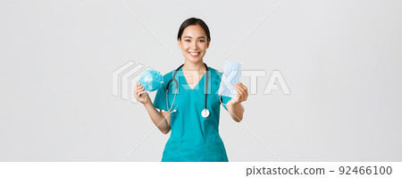 Covid-19, coronavirus disease, healthcare workers concept. Pleasant female physician, asian doctor in scrubs showing respirator and medical mask, provide staff with personal protective equipment 92466100