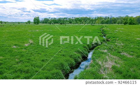 Small stream runs through a green grassy landscape Small stream runs through a green grassy landscape 92466115