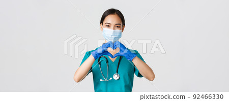 Covid-19, coronavirus disease, healthcare workers concept. Close-up of charming smiling asian female doctor, physician in medical mask and rubber gloves, provide care for patients, show heart gesture 92466330