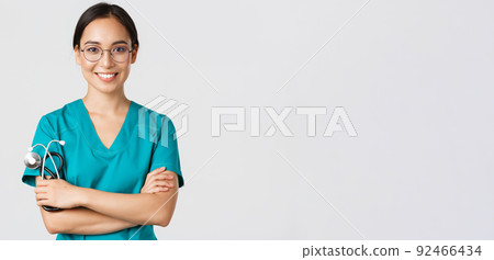 Covid-19, coronavirus disease, healthcare workers concept. Close-up of confident professional female doctor, nurse in glasses and scrubs standing white background, cross arms 92466434