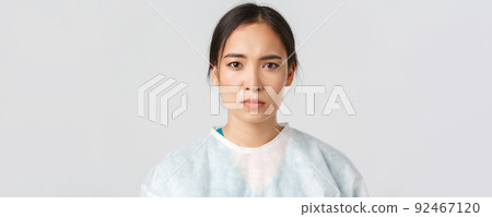 Covid-19, coronavirus disease, healthcare workers concept. Serious exhausted asian female doctor looking tired after shift at hospital, take-off personal protective equipment, have skin marks Covid-19, coronavirus disease, healthcare workers concept. Serious exhausted asian female doctor looking tired after shift at hospital, take-off personal protective equipment, have skin marks 92467120