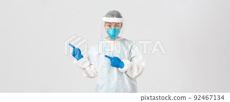 Covid-19, coronavirus disease, healthcare workers concept. Surprised female asian doctor, physician in medical respirator and personal protective equipment pointing upper left corner Covid-19, coronavirus disease, healthcare workers concept. Surprised female asian doctor, physician in medical respirator and personal protective equipment pointing upper left corner 92467134