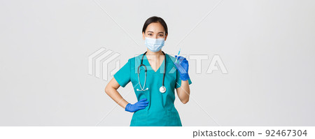 Covid-19, coronavirus disease, healthcare workers concept. Smiling confident asian female nurse in scrubs and medical mask, holding syringe with vaccine, doing vaccination shot, white background Covid-19, coronavirus disease, healthcare workers concept. Smiling confident asian female nurse in scrubs and medical mask, holding syringe with vaccine, doing vaccination shot, white background 92467304