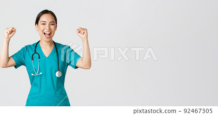 Covid-19, healthcare workers and preventing virus concept. Successful confident asian female doctor or nurse in scrubs fist pump and shouting yes, rejoicing, encourage herself, aim for victory Covid-19, healthcare workers and preventing virus concept. Successful confident asian female doctor or nurse in scrubs fist pump and shouting yes, rejoicing, encourage herself, aim for victory 92467305