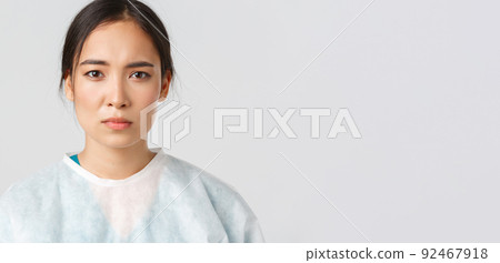 Covid-19, coronavirus disease, healthcare workers concept. Serious exhausted asian female doctor looking tired after shift at hospital, take-off personal protective equipment, have skin marks Covid-19, coronavirus disease, healthcare workers concept. Serious exhausted asian female doctor looking tired after shift at hospital, take-off personal protective equipment, have skin marks 92467918
