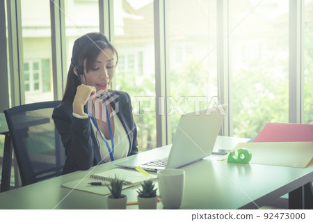 Asian female operator is talking on the phone to service client in the telemarkerting office. Asian female operator is talking on the phone to service client in the telemarkerting office. 92473000