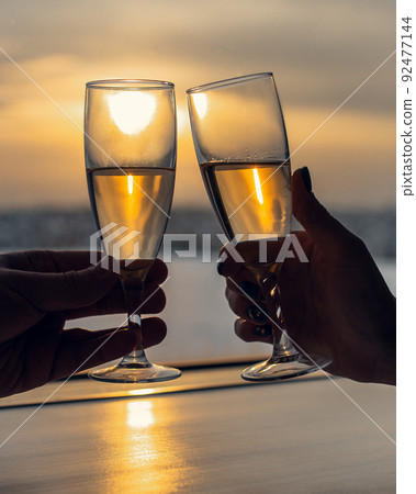 Two glasses with champagne clink glasses against the background of window on sunset 92477144