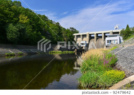 A dam on the Brno Reservoir by the Svratka River with a small power plant. Beautiful sunny summer day in nature. 92479642