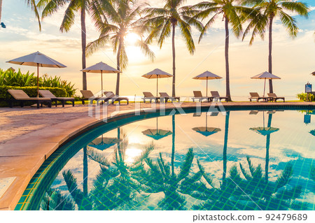 Beautiful luxury umbrella and chair around outdoor swimming pool in hotel and resort with coconut palm tree on sunset  or sunrise sky 92479689