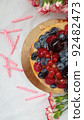 Berry cake. Cheesecake with cherries, raspberries, currants and blueberries. Birthday cake. Half of a cheesecake, pink candles and red flowers on a white background. Photo for stories. 92482473