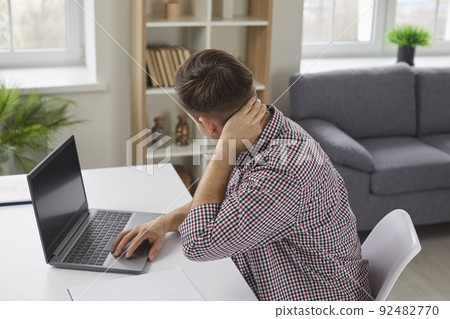 Tired man feels pain in his neck and back of his head after working on laptop computer 92482770