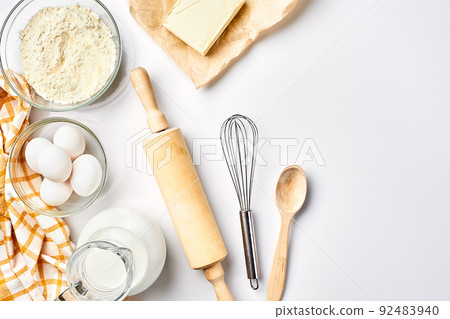 Preparation of the dough. A measurement of the amount of ingredients in the recipe. Ingredients for the dough: flour, eggs, rolling pin, whisk, milk, butter, cream. Top view, space for text Preparation of the dough. A measurement of the amount of ingredients in the recipe. Ingredients for the dough: flour, eggs, rolling pin, whisk, milk, butter, cream. Top view, space for text 92483940