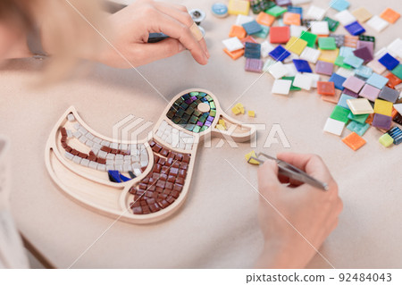 Workplace of the mosaic master: women's hands holding tool for mosaic details in the process of making a mosaic Workplace of the mosaic master: women's hands holding tool for mosaic details in the process of making a mosaic 92484043