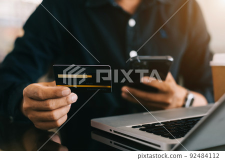 Closeup male holding hand credit card. Businessman use smartphone online payments shopping touching screen mobile phone name numbers. 92484112