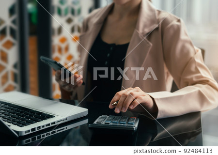 Investors are calculating on calculator investment costs and holding smartphone in hand. Investors are calculating on calculator investment costs and holding smartphone in hand. 92484113
