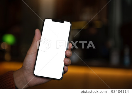 Hand holding white mobile phone with blank white screen in cafe. Hand holding white mobile phone with blank white screen in cafe. 92484114