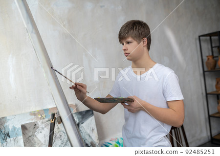 A boy with down syndrome painting in the studio and looking involved A boy with down syndrome painting in the studio and looking involved 92485251