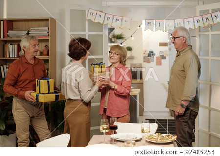 Happy mature couple giving packed and wrapped giftboxes to aged woman 92485253